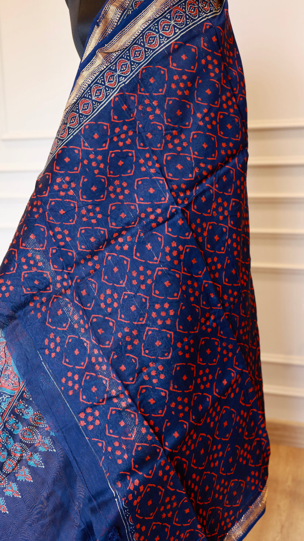 Close-up drape of Titafu's Indigo Maheshwari silk saree showing red geometric handblock prints and a fine gold zari border.