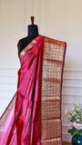 A deep Rani pink silk saree with an ornate gold zari border, draped on a black mannequin torso against a cream paneled wall.