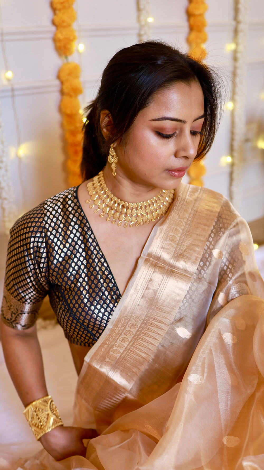 Close-up detail shot showing the rich woven zari pallu border of the metallic gold tissue silk saree and contrasting dark brocade blouse.