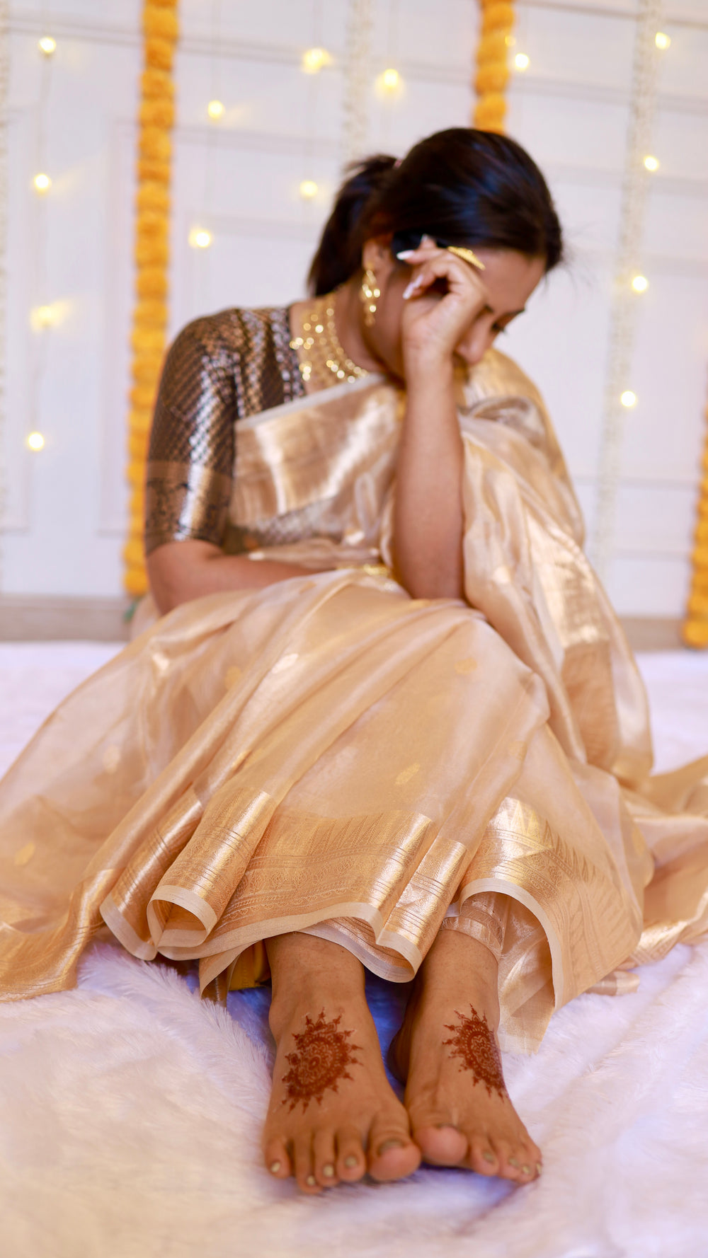 Seated lifestyle shot showing the fluid drape and soft metallic shimmer of the gold Banarasi tissue silk fabric.