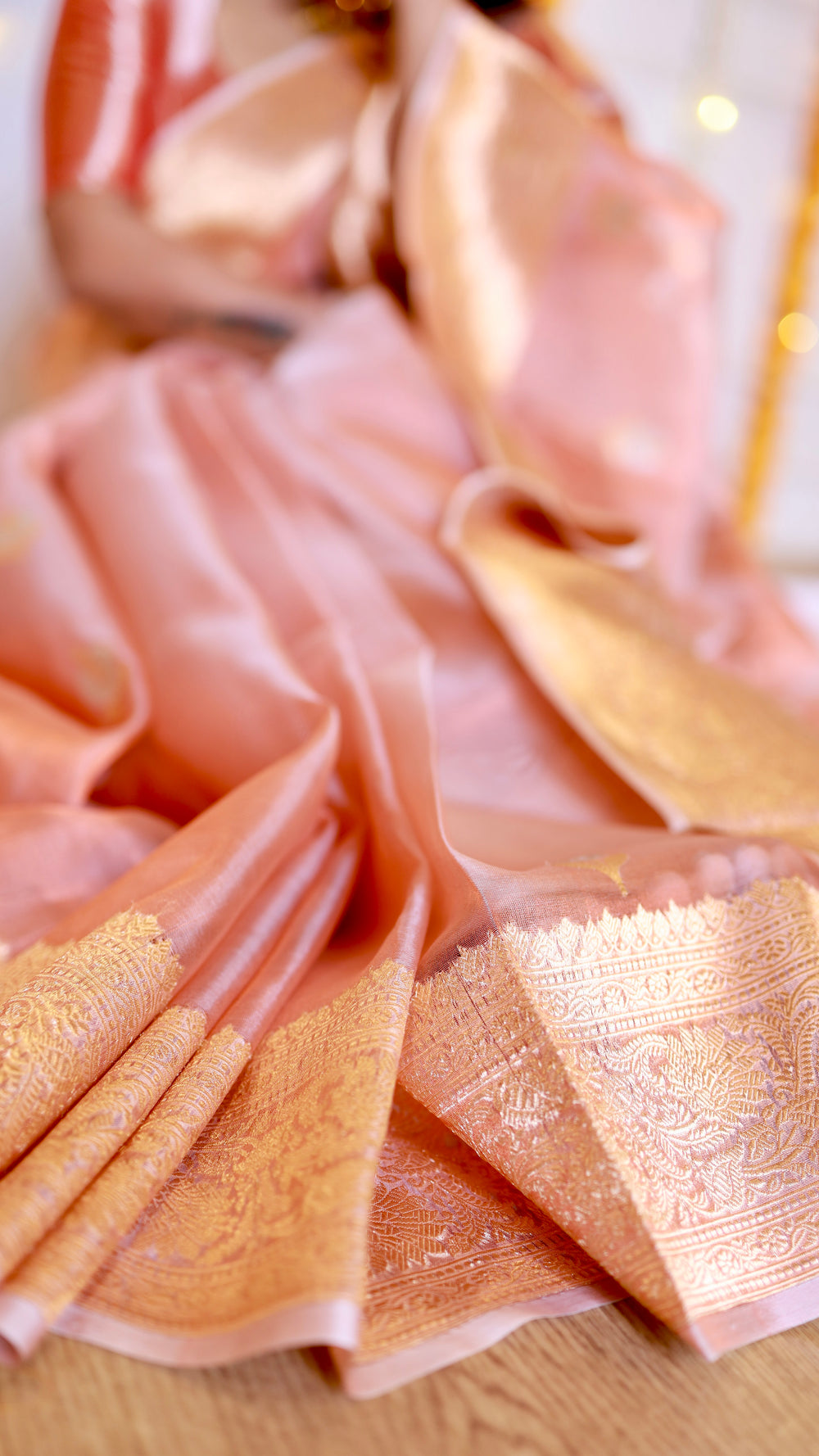 High-angle detail shot showcasing the rich floral gold zari border folds on the peach tissue saree.