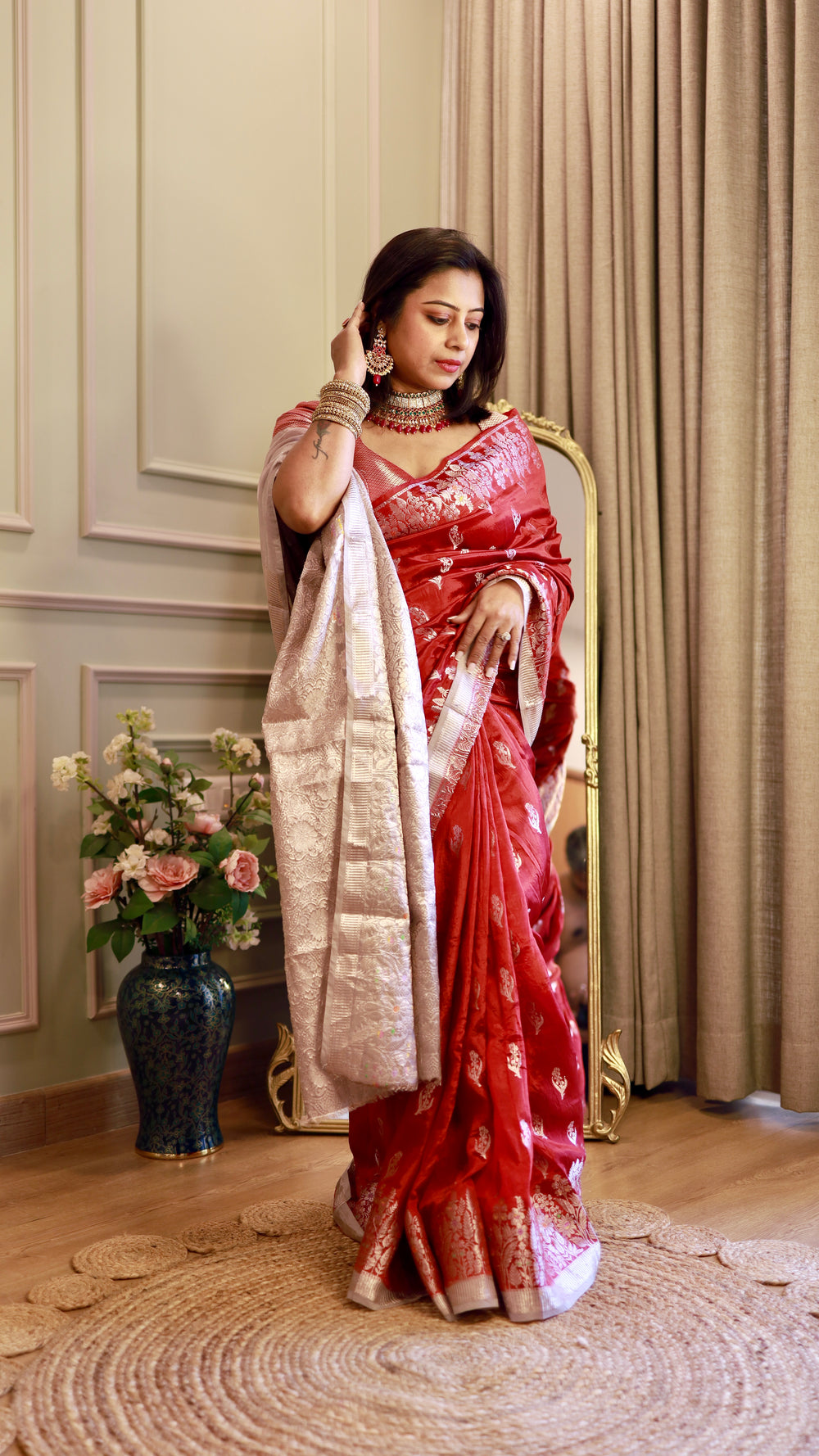 Front view of model holding her hair, displaying the graceful drape and subtle sheen of the Crimson Red Georgette Banarasi Saree with a silver zari border.