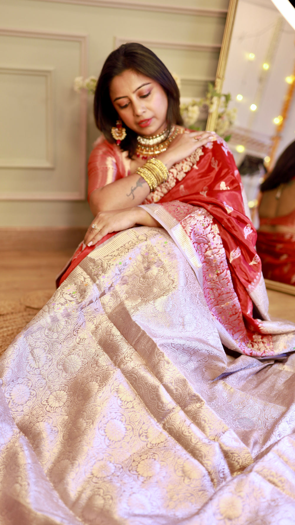 Model seated showing the full view of the champagne-silver tissue woven pallu contrasting against the red Banarasi georgette saree.