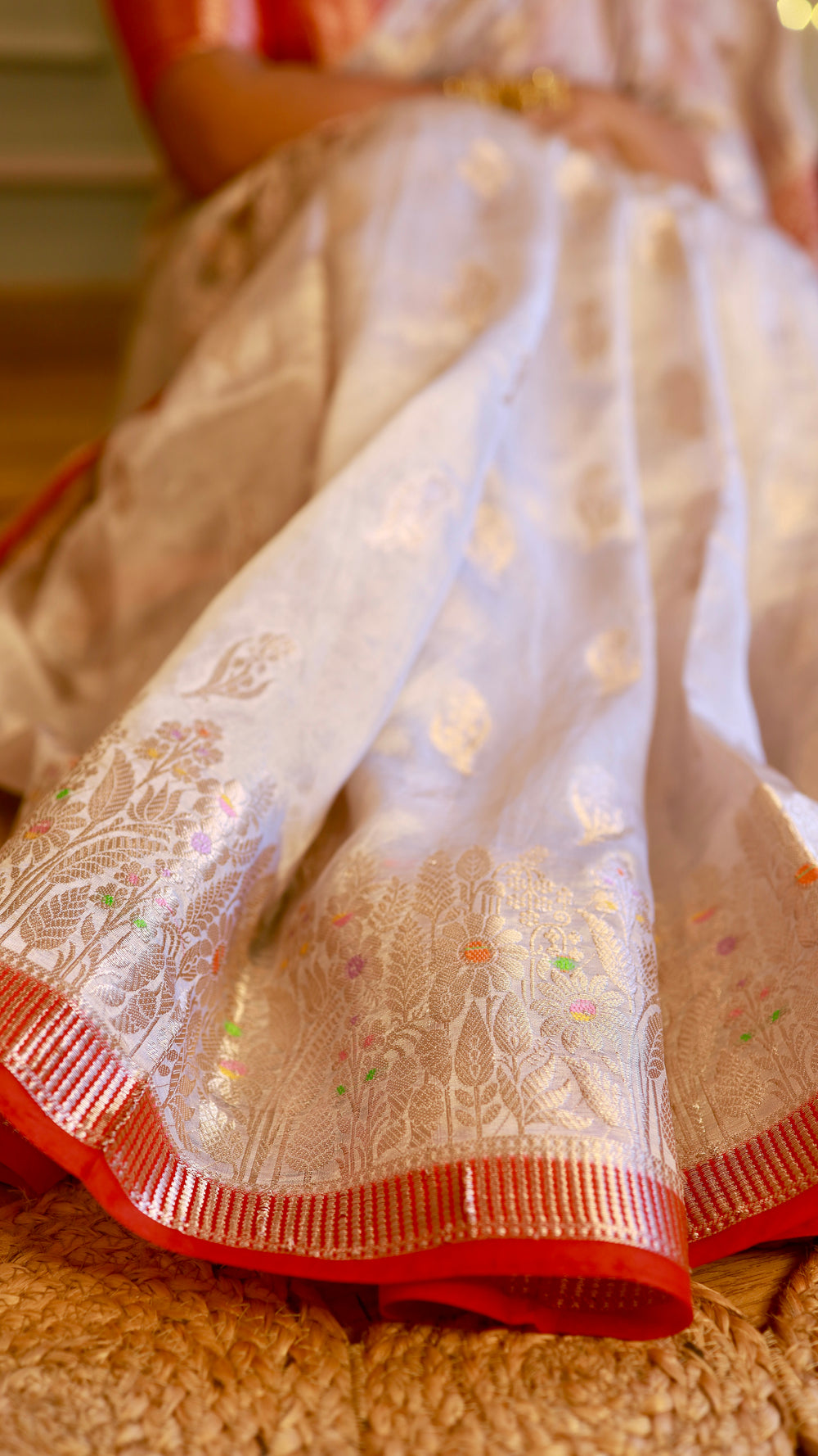 Macro detail shot of the off-white saree pleats featuring delicate gold woven bootis and floral zari border.