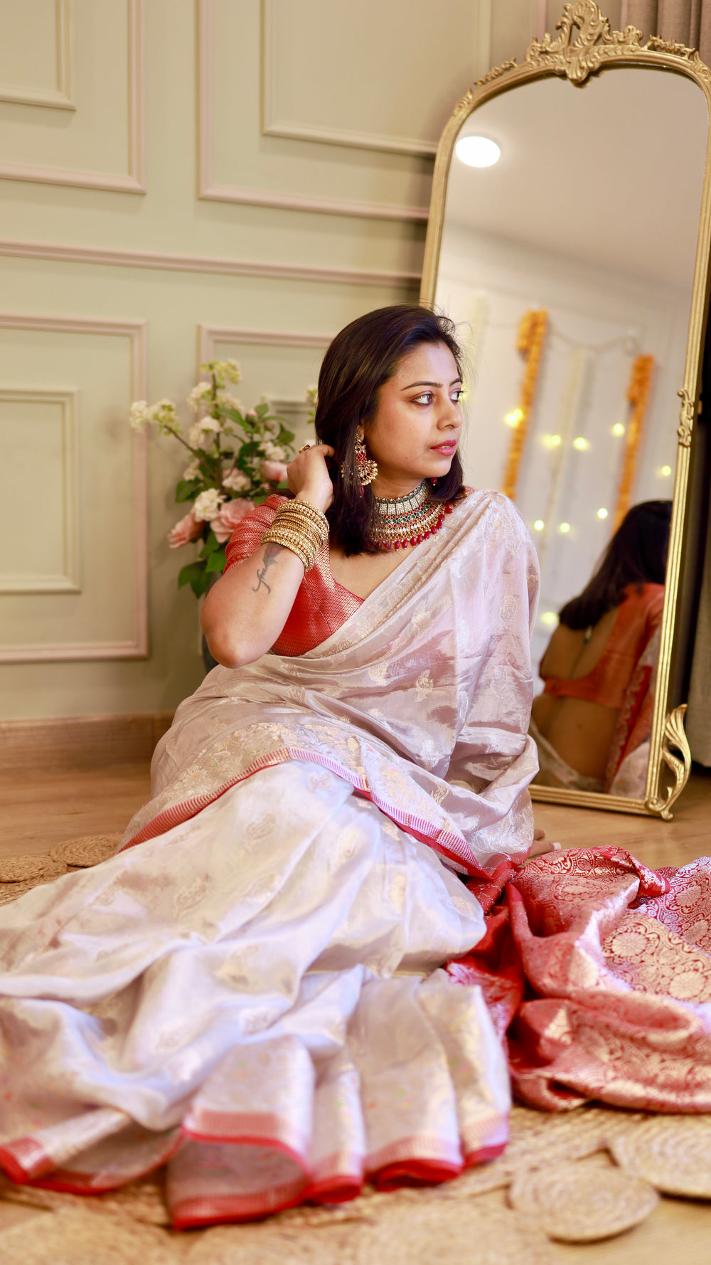Side profile view of a model wearing an off-white georgette saree with a metallic red blouse and gold jewelry.