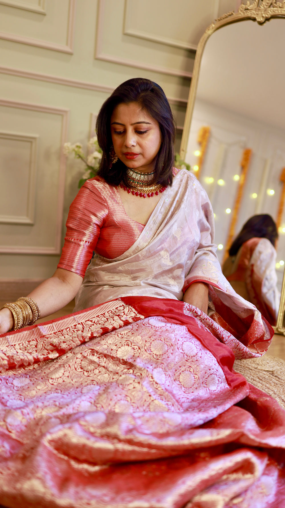 Woman seated draped in an off-white pure georgette Banarasi saree showing off the intricate crimson red zari pallu.