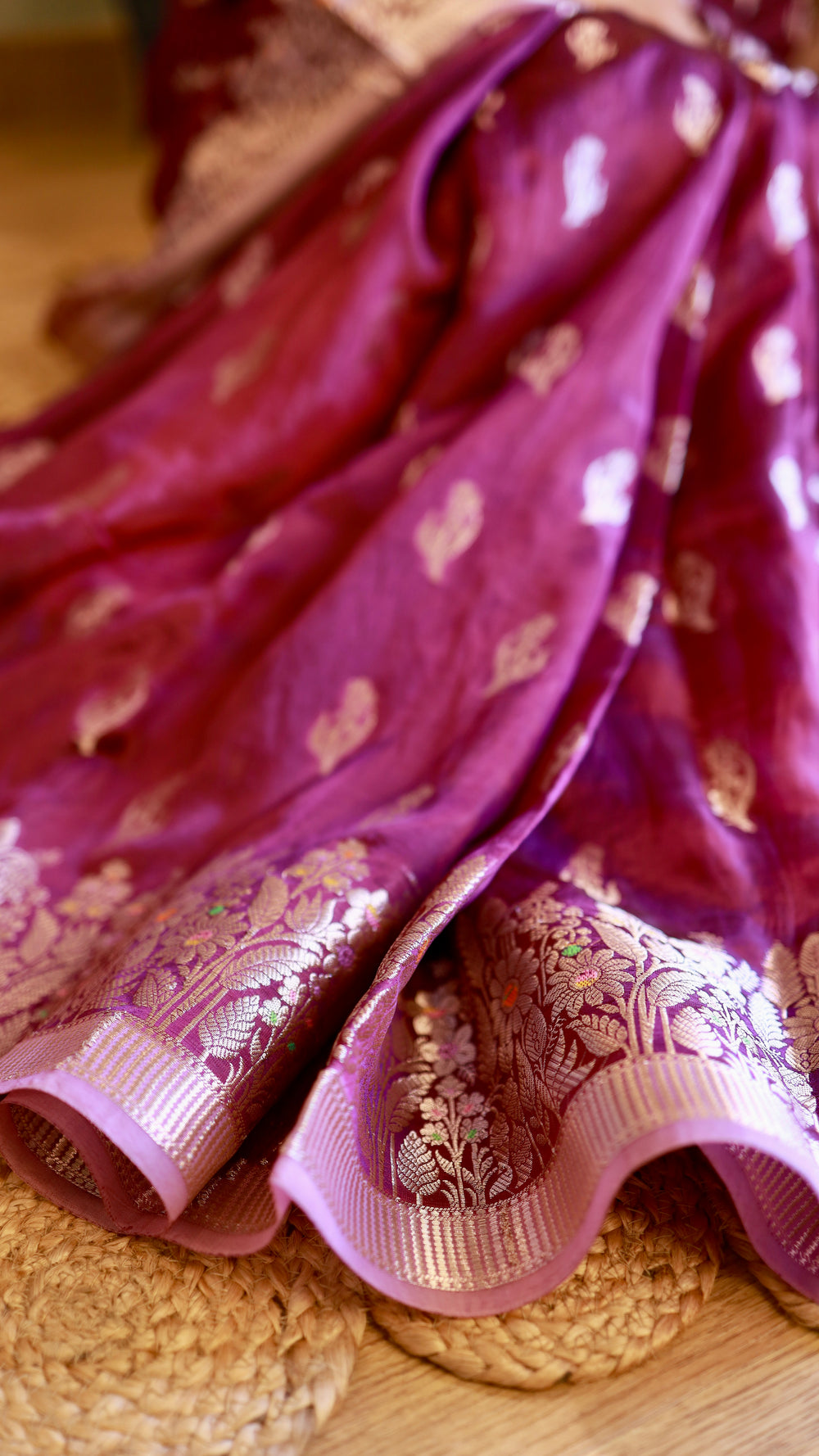 Close-up detail of a royal purple georgette Banarasi saree showing delicate silver zari leaf motifs and woven floral border.