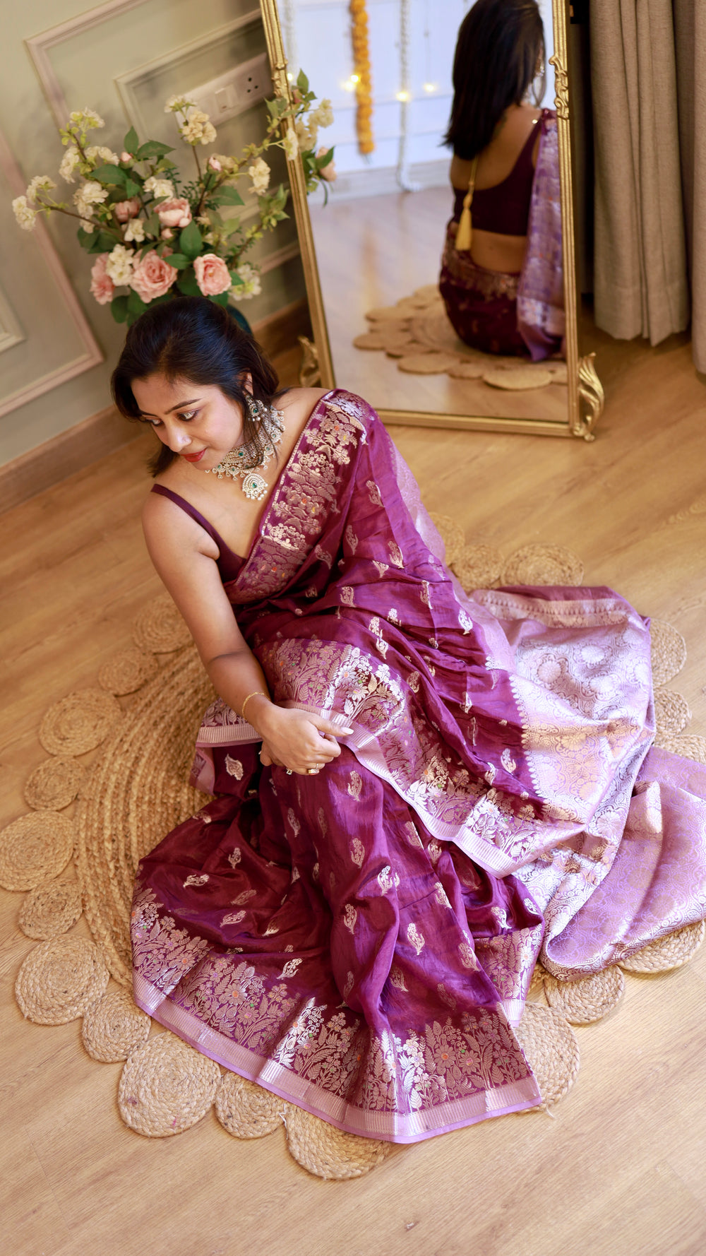 Top-angle view of a woman seated on a woven rug wearing a rich purple silver zari georgette Banarasi saree.