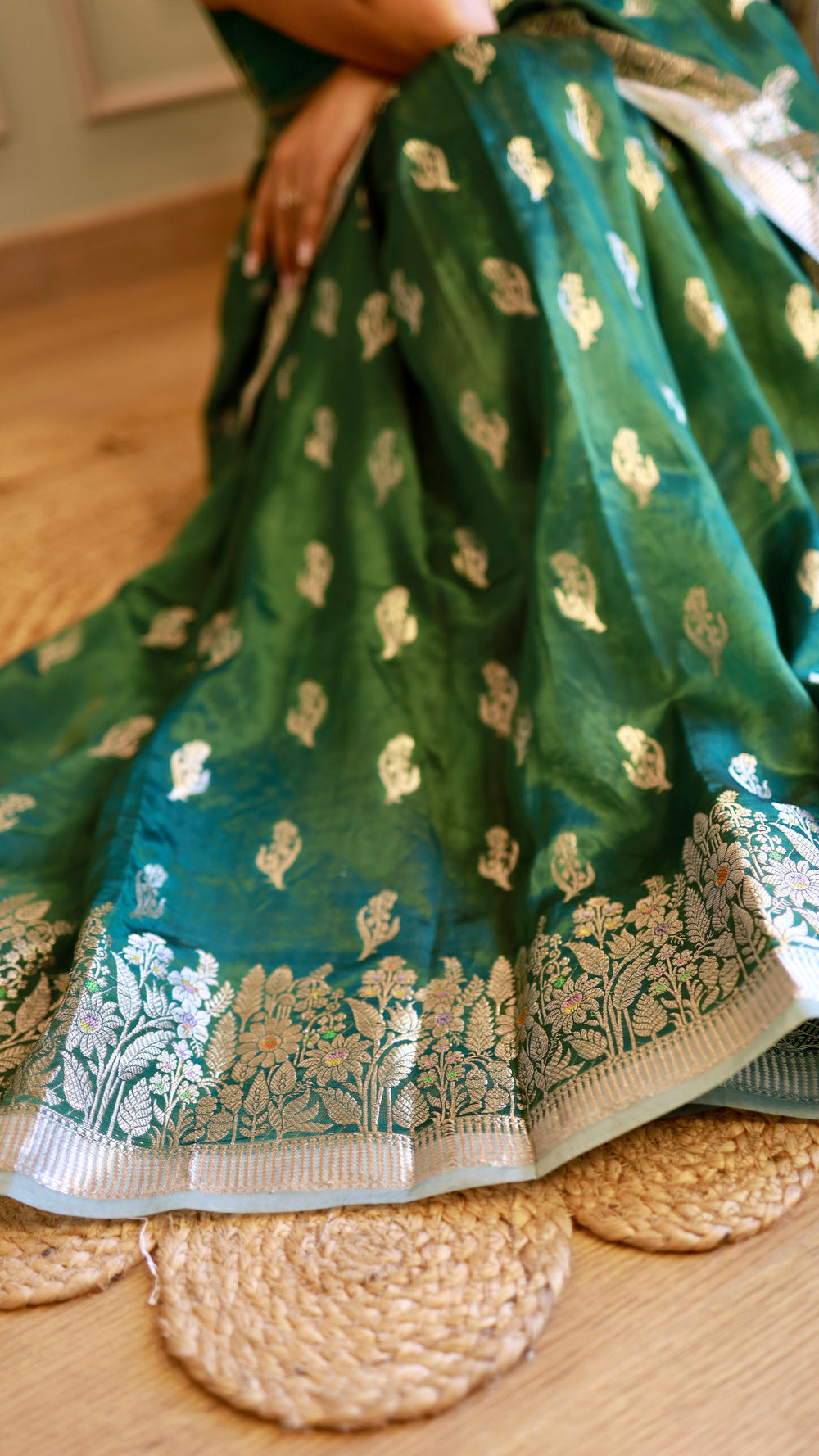 Close-up of emerald green georgette saree pleats displaying silver floral zari motifs and detailed floral border.