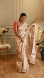 Woman wearing full-length champagne Ivory Munga Contrast Banarasi Saree paired with a coral brocade blouse, standing on a jute rug.