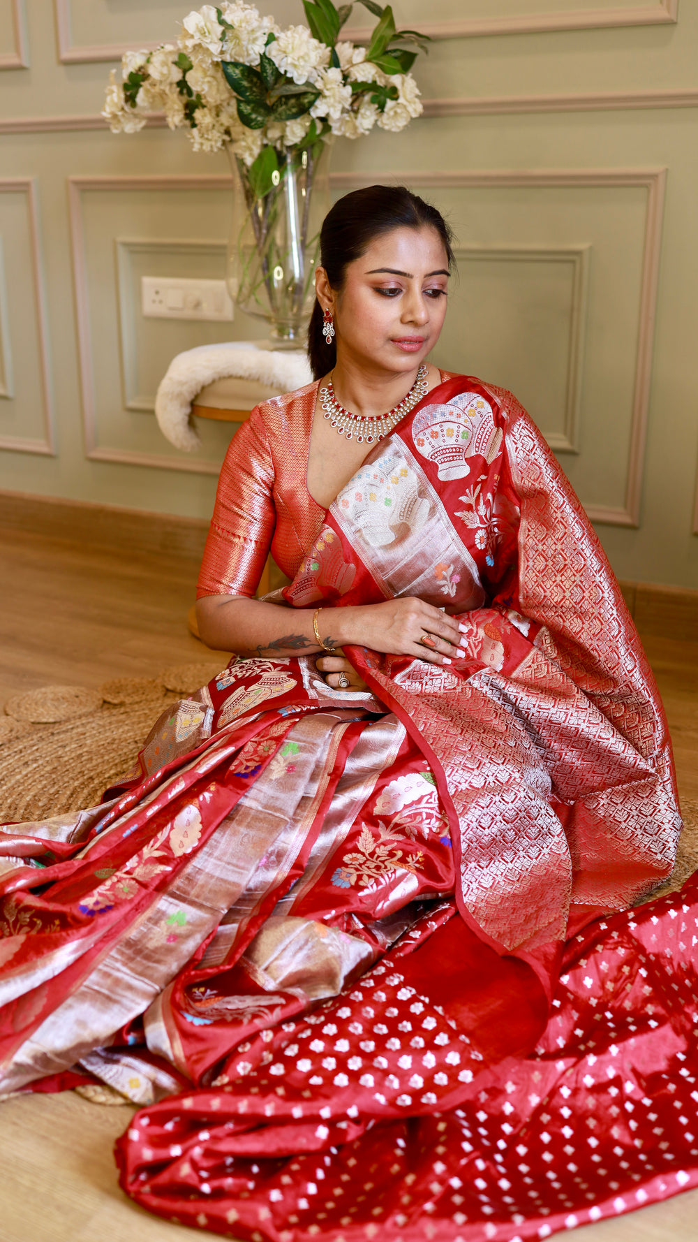 Model seated on the floor demonstrating the drape and detailed pallu motifs of the crimson Munga contrast Banarasi silk saree.