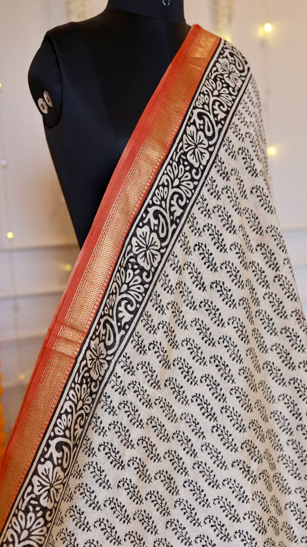 Close-up view of off-white Maheshwari silk saree showing black floral block print and rust red gold zari border