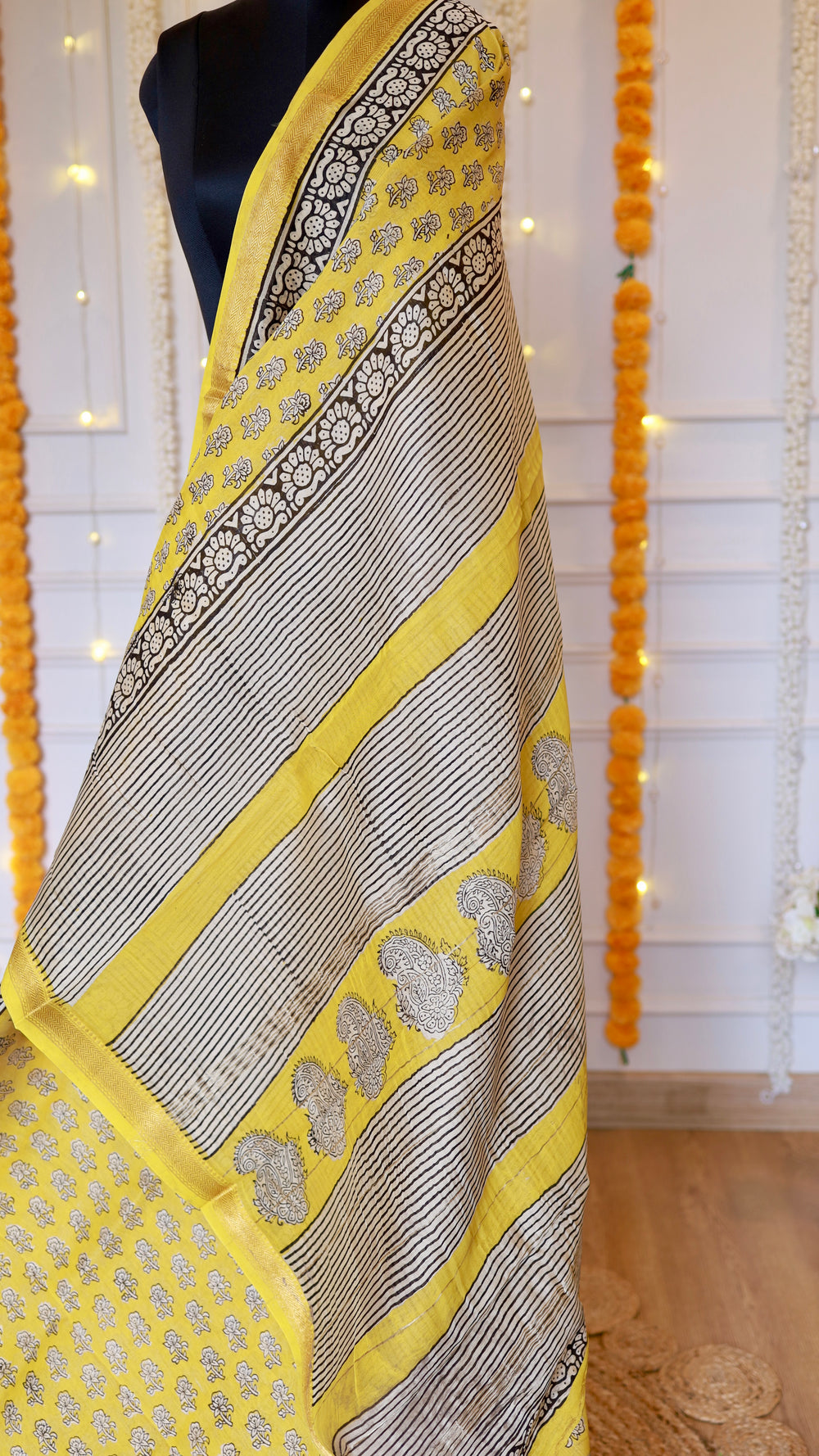 Yellow handblock printed Maheshwari silk saree drape showing geometric striped pallu and black floral woven zari border