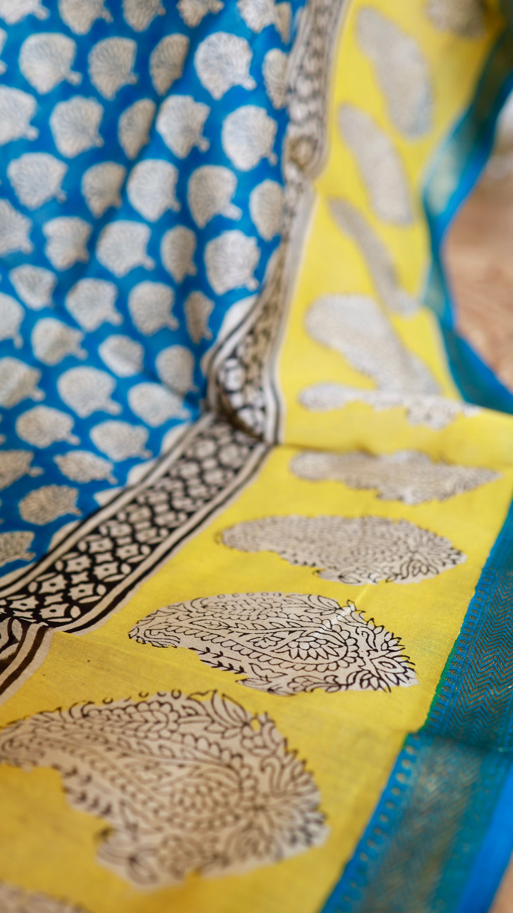 Close-up texture shot of Maheshwari Silk Saree displaying blue tree motifs and yellow paisley border detail.