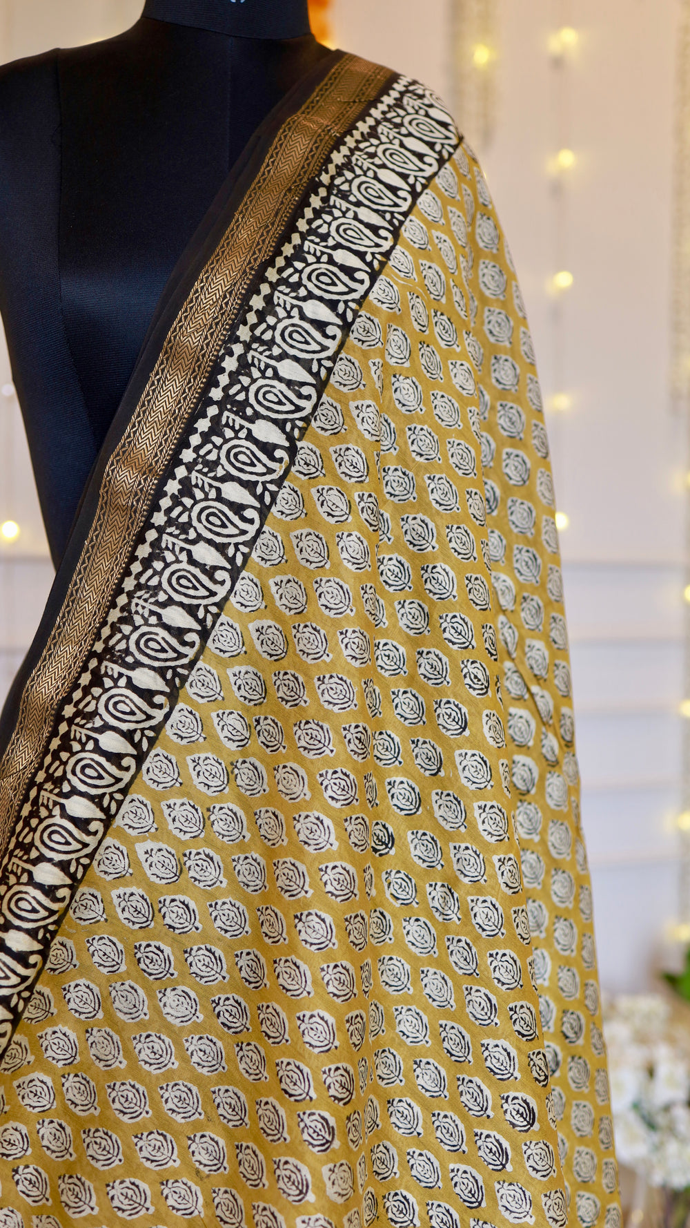 Close-up view of mustard yellow Maheshwari silk saree fabric showing detailed leaf block print and woven metallic zari edge.
