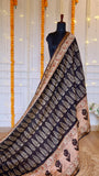 Full pleat and drape view of charcoal black Maheshwari silk saree with white leaf block prints, ornate red pallu border, and gold zari hem.