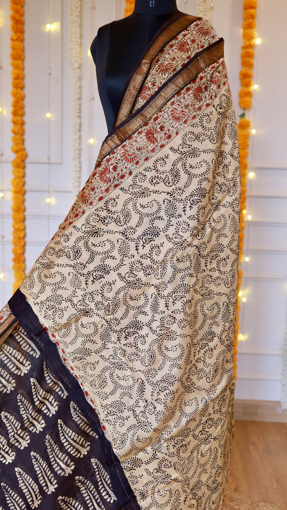 Hand block printed Maheshwari silk saree draped on mannequin featuring off-white paisley body, red floral borders, and woven golden zari edging.