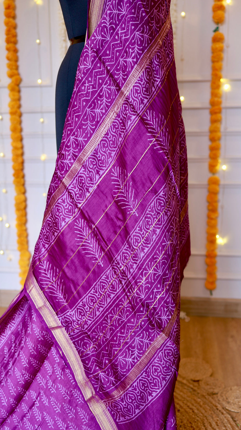 Detailed view of the ornate pallu design with geometric wave patterns, printed foliage, and metallic gold zari striping.
