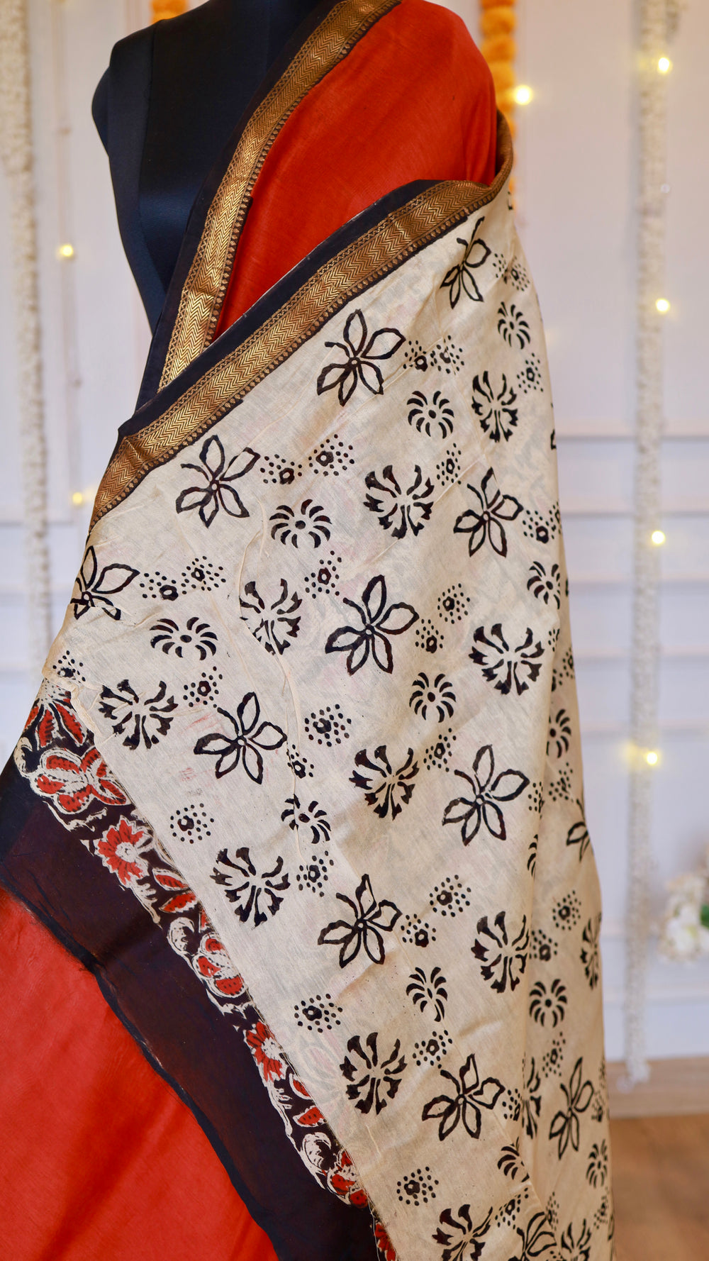 Display of off-white pallu with black block print motifs contrasted against the rust red Maheshwari silk saree.