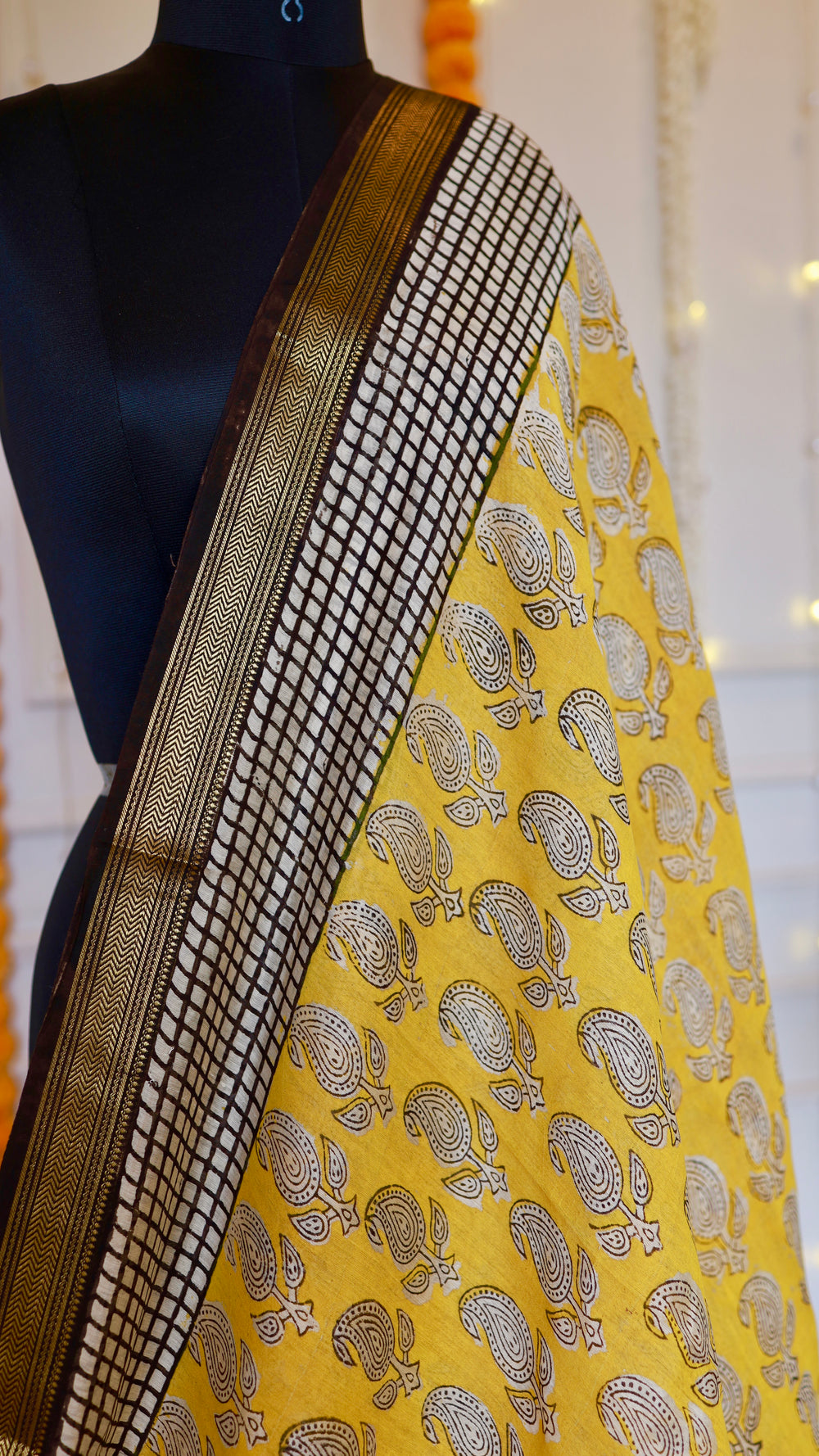 Upper shoulder drape of Mustard Yellow Maheshwari Silk Saree displaying paisley block prints and geometric grid border.