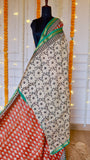 Rust Red Maheshwari Silk Saree draped on a mannequin showing off-white floral block-printed pleats and emerald zari border.