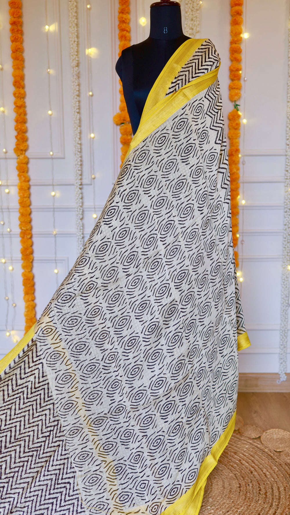 Maheshwari Silk Saree featuring black and off-white geometric block print body with a bright yellow zari border draped on a mannequin.