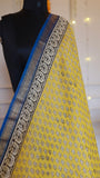 Close-up shot of mustard yellow body fabric featuring traditional block print and fine woven zari border detail.