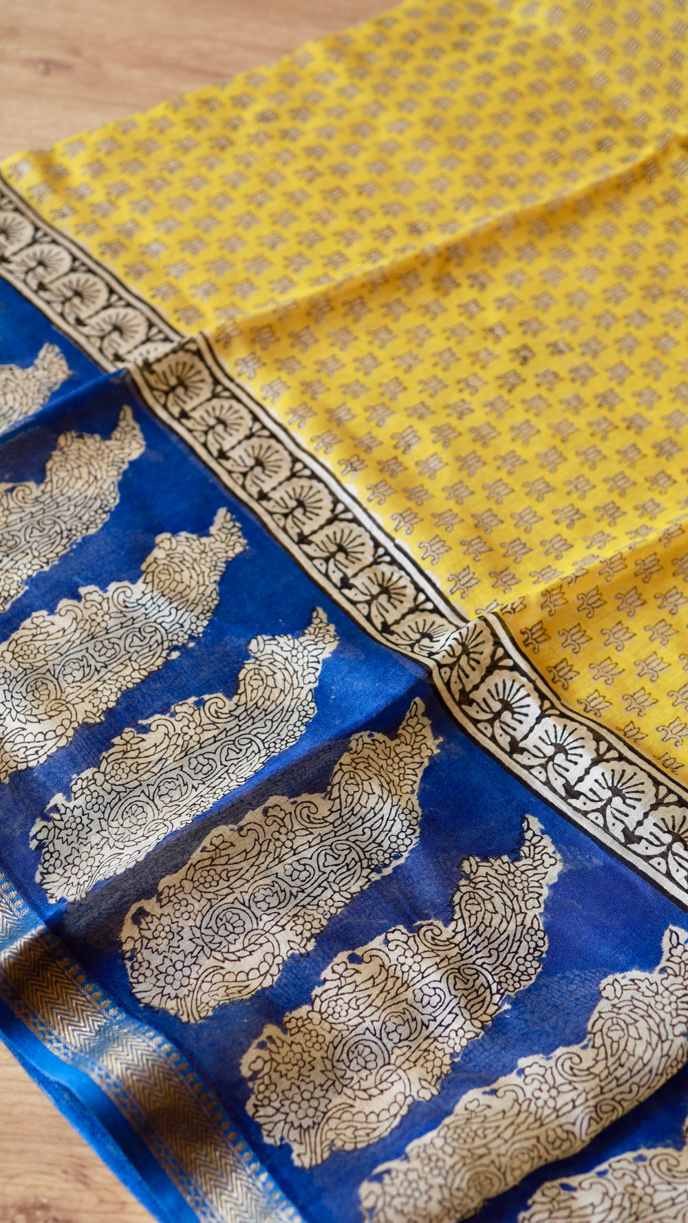 Detailed flat lay showing contrast between mustard yellow body print and royal blue pallu with intricate paisley motifs.