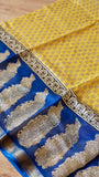 Detailed flat lay showing contrast between mustard yellow body print and royal blue pallu with intricate paisley motifs.