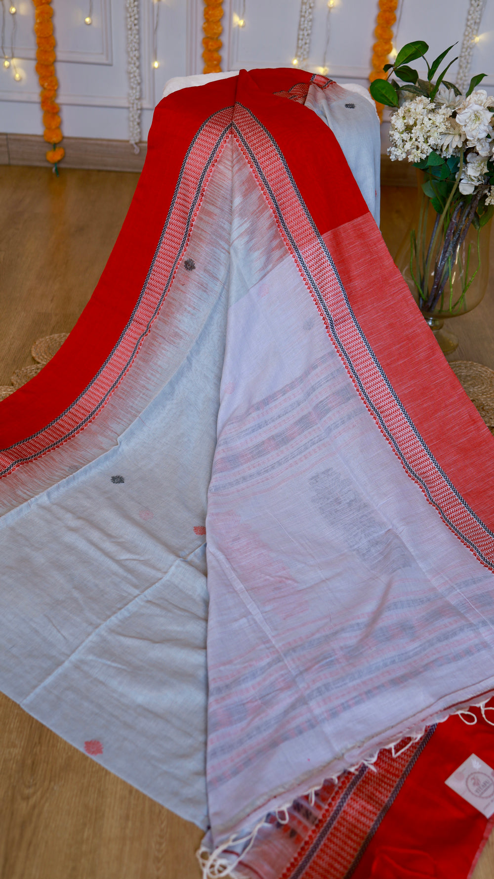Detailed fold of the off-white cotton Bomkai saree featuring the red border edging and intricate hand-knotted tassel fringe at the edge.