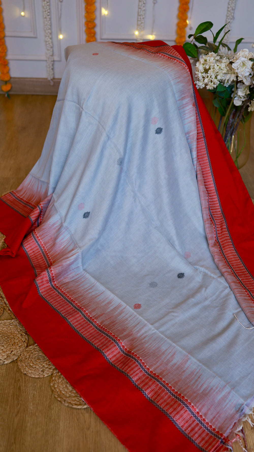 Off-white cotton Bomkai saree draped with a vibrant crimson red temple border and small woven extra-weft floral sprigs across the body.