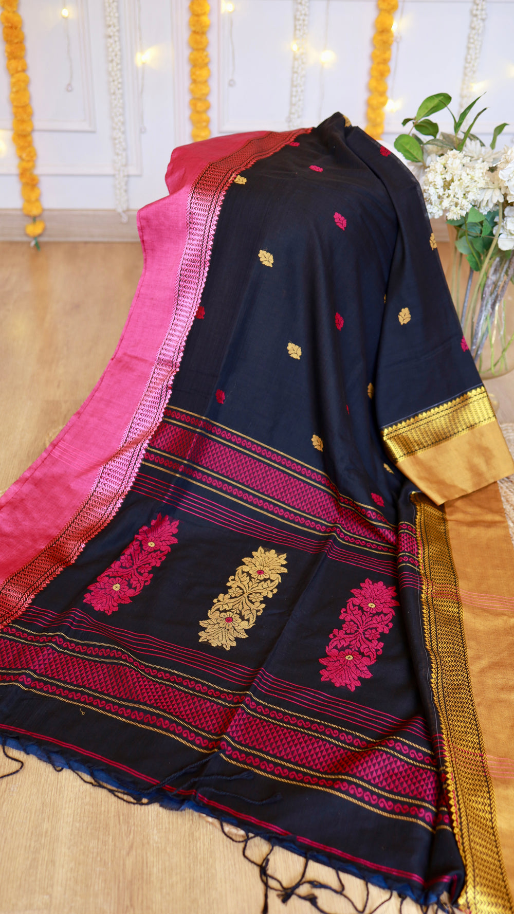 Alt Text: Midnight black cotton Bomkai saree featuring crimson woven pallu motifs, gold zari border, and matching tassels on display