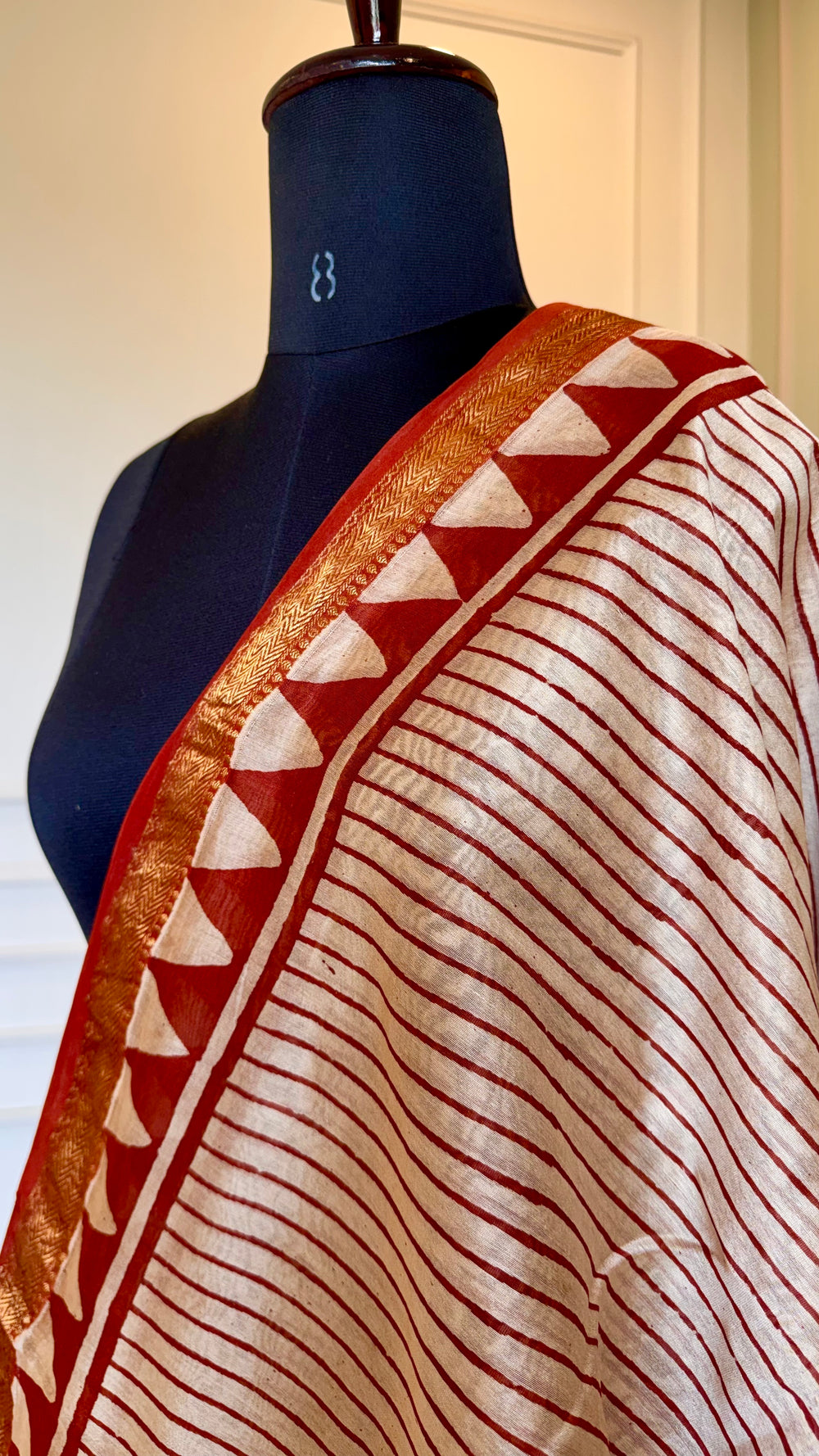 Close-up of Maheshwari Silk Saree fabric showing the intricate gold zari border and geometric triangle patterns.