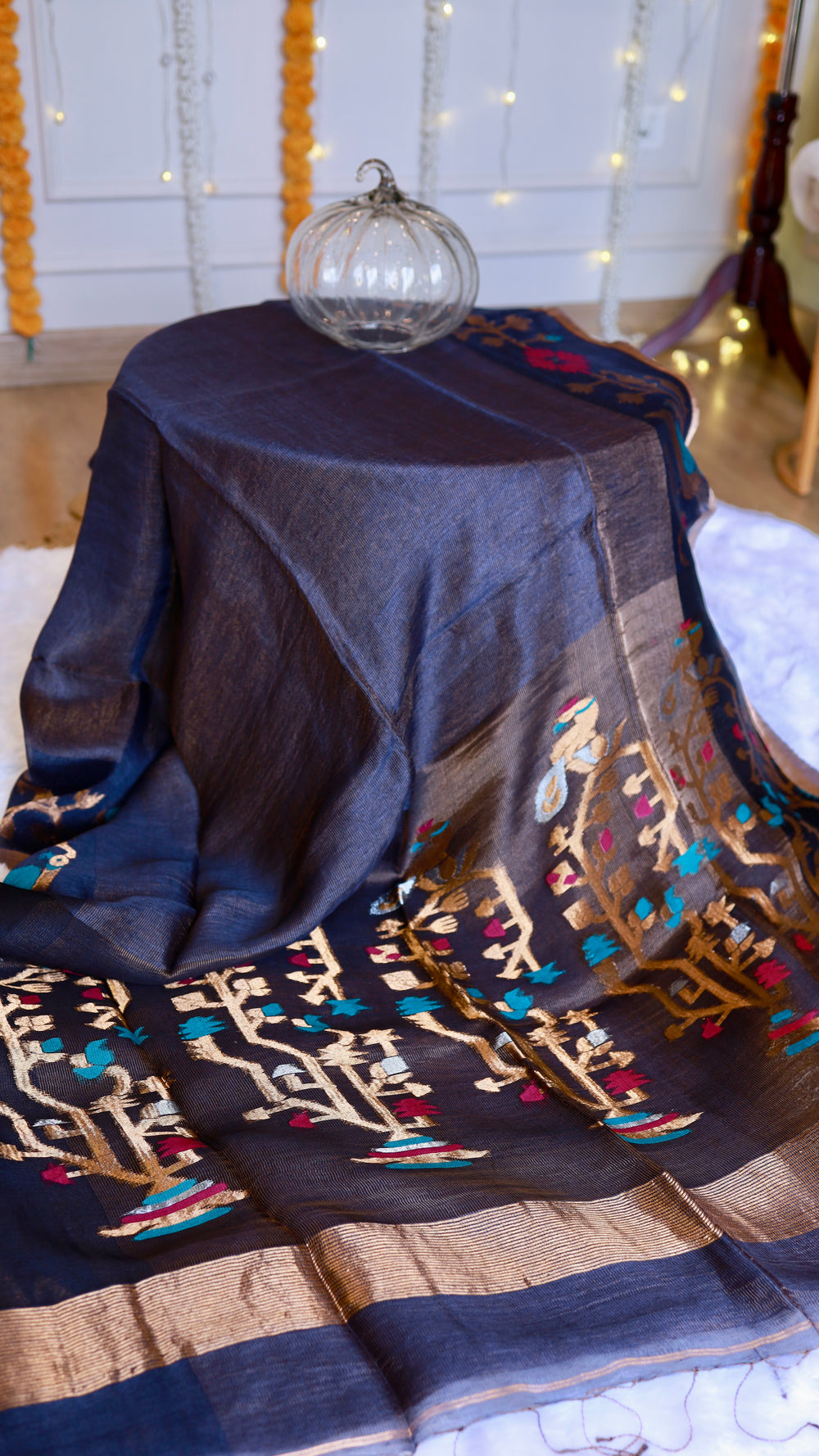 Midnight blue pure silk linen saree draped over display showcasing golden tree motifs on pallu and subtle shimmer.