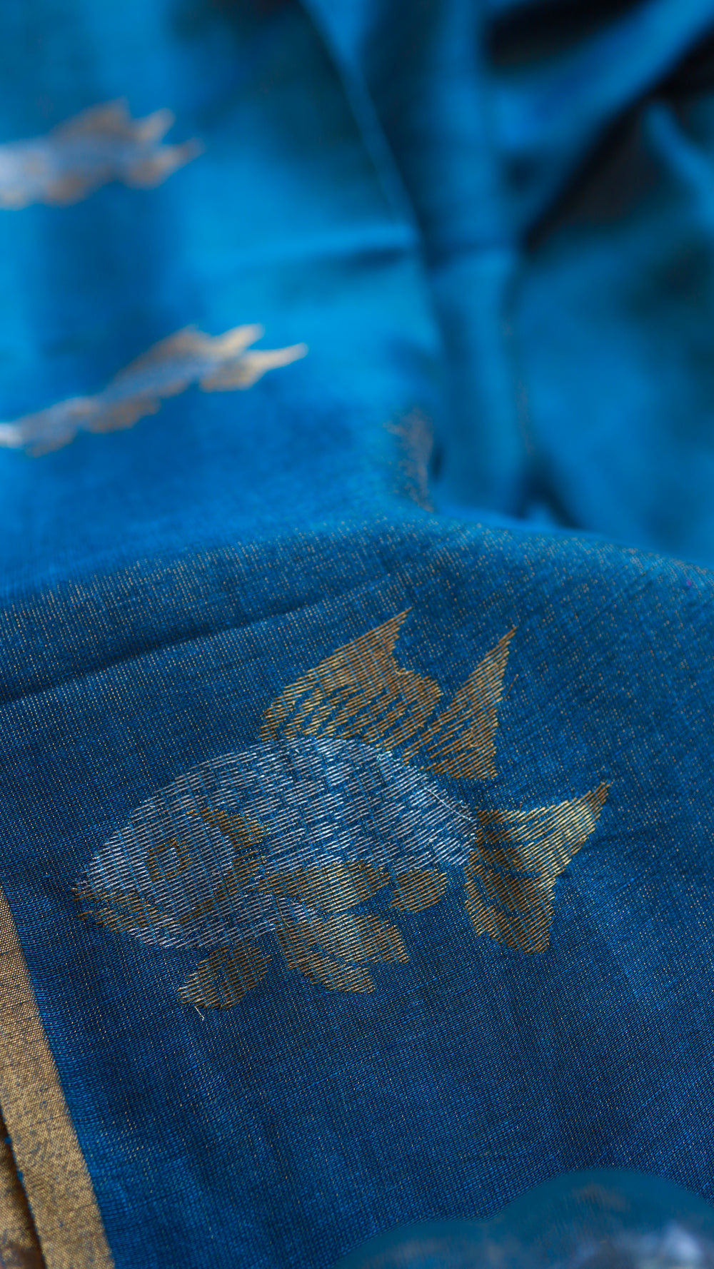 Macro shot of hand-woven dual-tone zari fish motif on textured peacock blue Pure Silk Linen fabric.