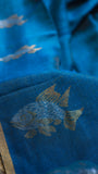 Macro shot of hand-woven dual-tone zari fish motif on textured peacock blue Pure Silk Linen fabric.
