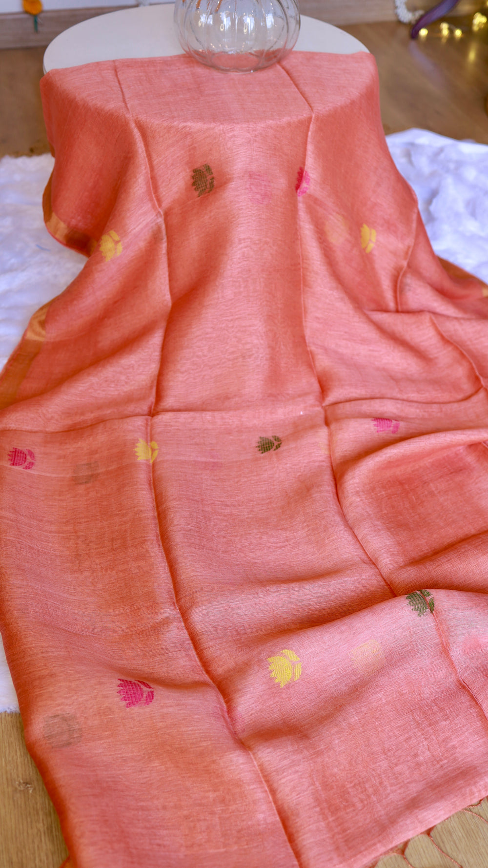 Full view of draped peach silk linen saree displayed on a table highlighting scattered floral buttas and gold border