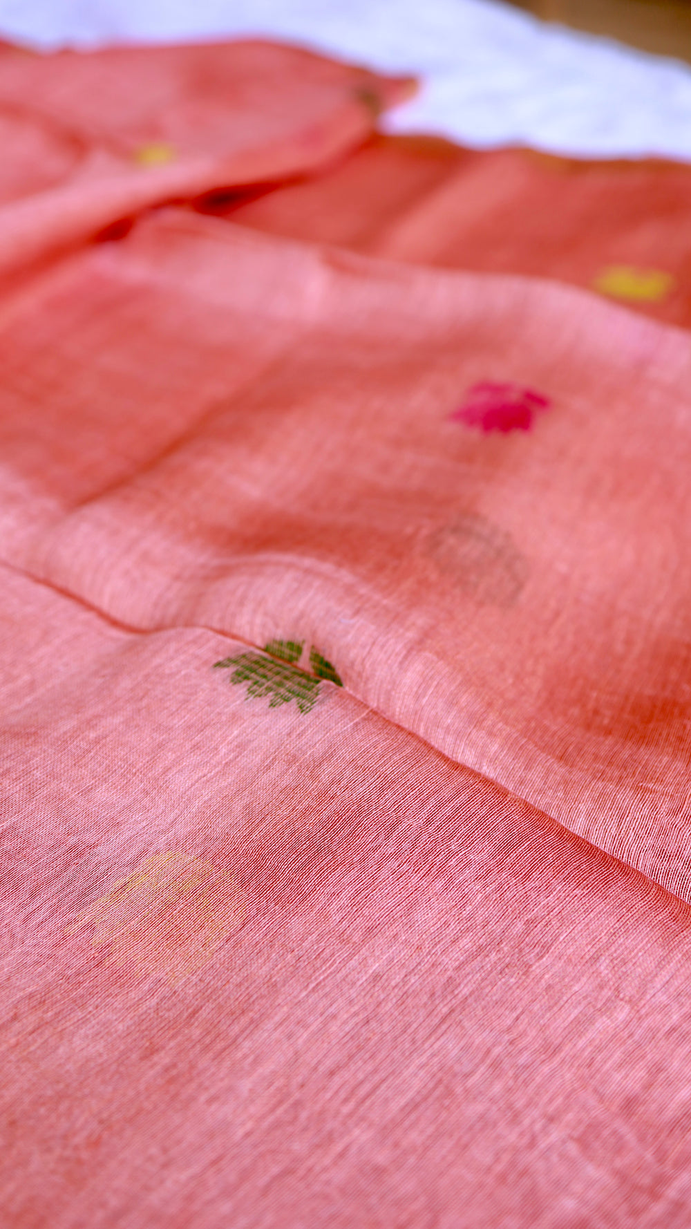 Close-up texture of peach coral pure silk linen saree showing handwoven green, yellow, and pink lotus motifs