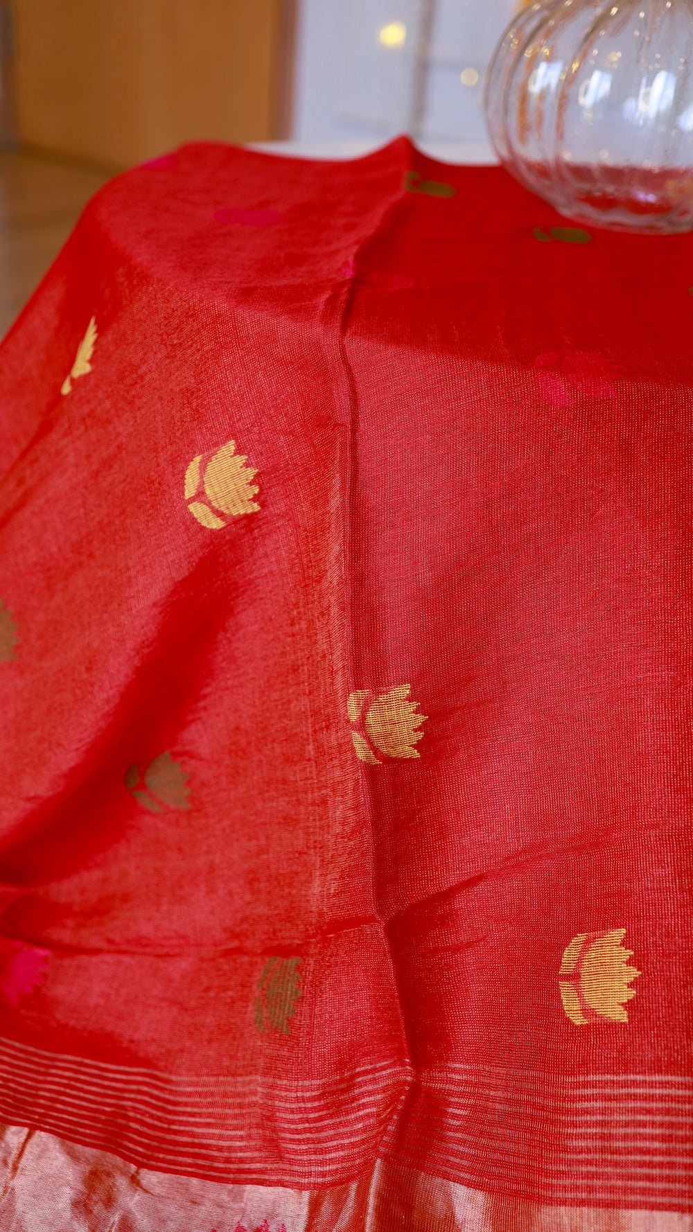 Macro detail view showing the delicate fabric texture and tiny gold and green buttas on the scarlet body of the saree.