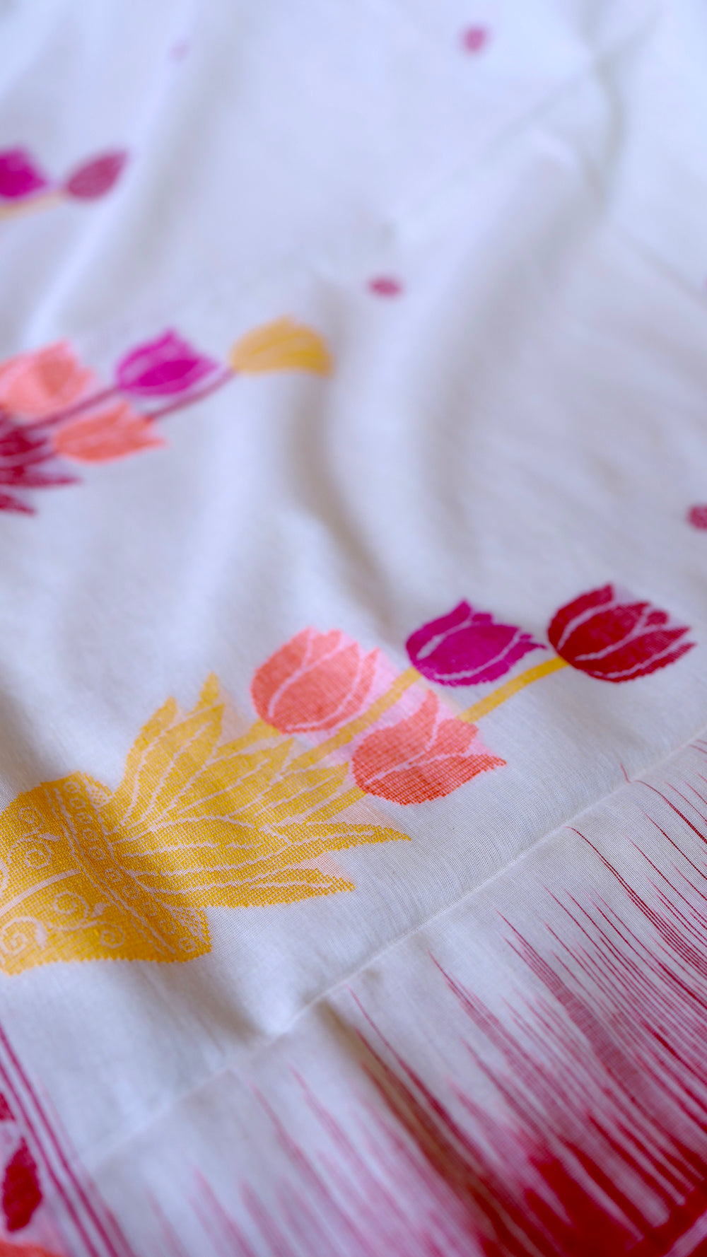 Macro close-up of vibrant pink, peach, and yellow tulip motifs woven on pure off-white khadi cotton yarn texture.
