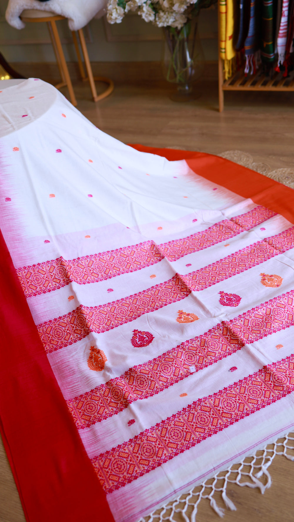 Overview of the white saree featuring multiple red/orange buttas and intricate red patterned stripes near the border, showing elegant fabric drape.