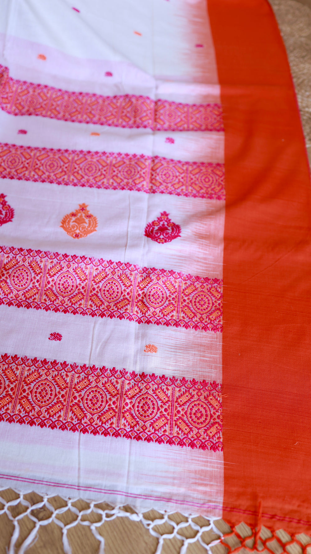 Detail shot highlighting the transition from the intricately woven red border patterns to the crisp orange selvedge/bottom edge of the Handwoven Saree.