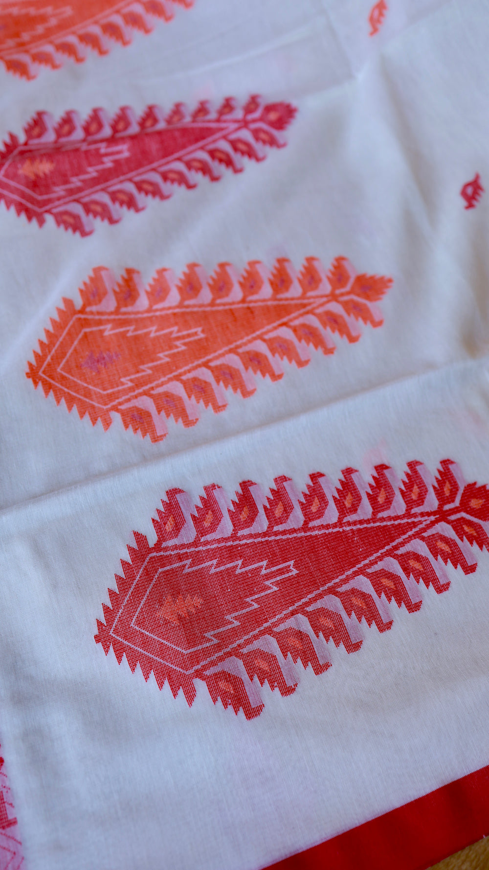 Detailed close-up of intricate woven red and orange paisley (kalka) motifs on off-white handspun Khadi cotton fabric.