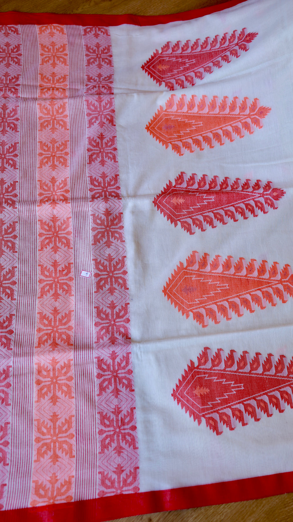 Close-up of pallu geometric floral borders and large red paisley weave on off-white Khadi saree.