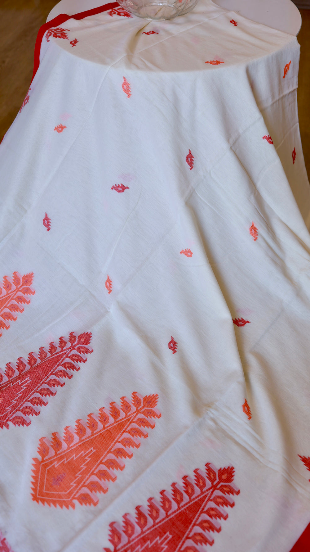 Off-white Khadi saree pallu draped gracefully over a round table showcasing crimson red woven motifs.