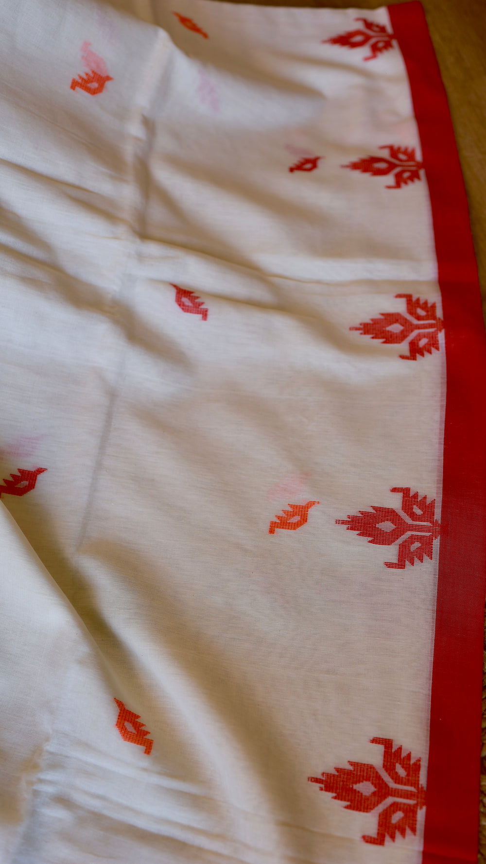 Close-up of saree pleats showing delicate red and orange floral woven bootis on pure off-white Khadi cotton.