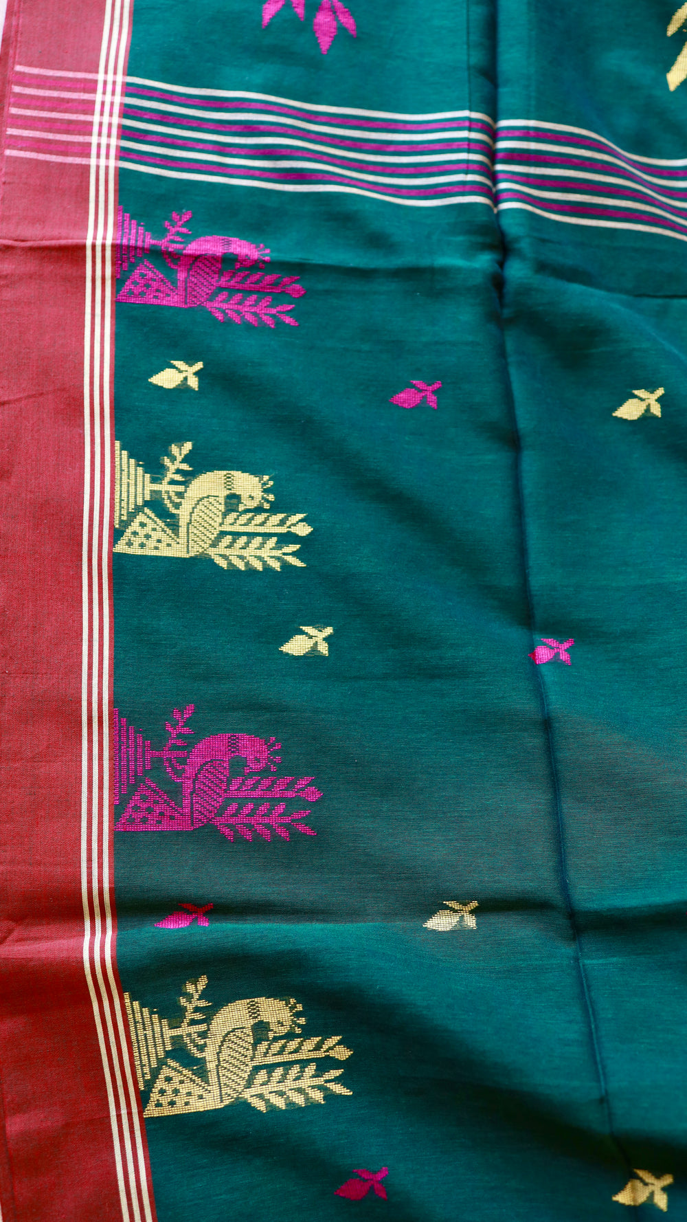 Medium shot focusing on a row of repeating golden zari peacock motifs woven into the deep green Khadi cotton fabric.