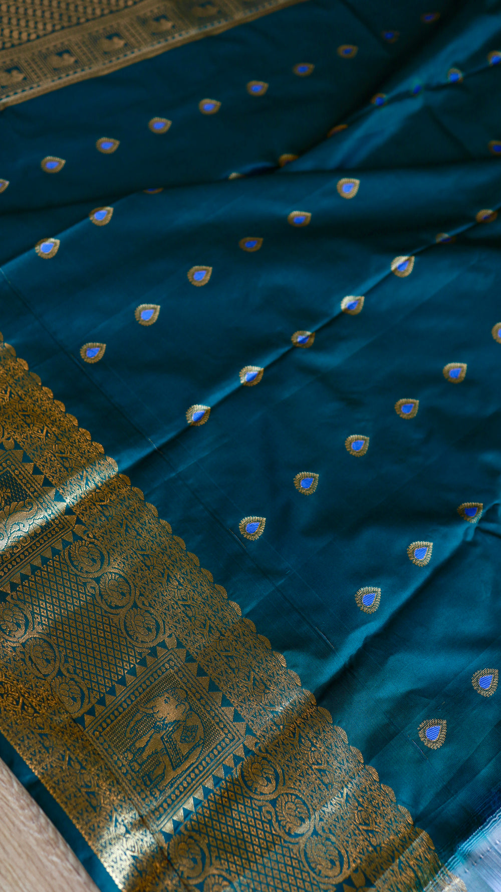 Unstitched blouse piece fabric in deep teal blue featuring small gold tear-drop butis and ornate zari border.