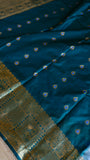 Unstitched blouse piece fabric in deep teal blue featuring small gold tear-drop butis and ornate zari border.