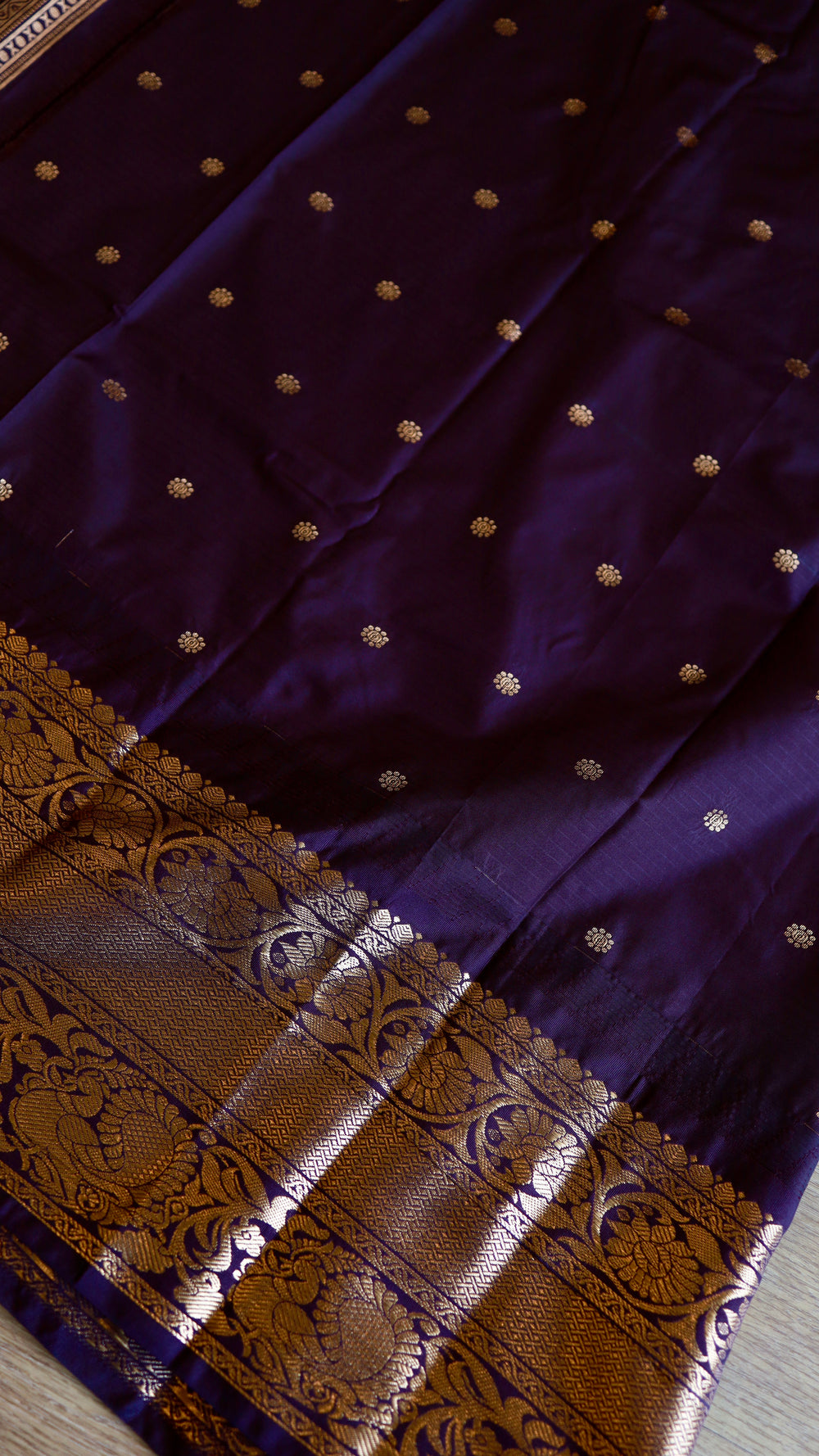 Close-up texture shot of the deep purple unstitched blouse piece with gold woven buttis and zari border included with the saree.